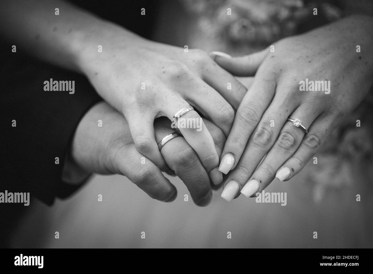 Grayscale shot of the bride and groom holding hands with their rings on the finger Stock Photo