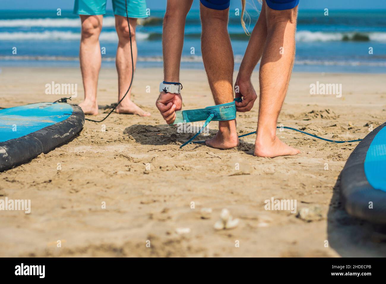 Summer time and active rest concept. Young surfer man beginner fastens leash across leg, going to surf on big barral waves on ocean, dresseed in Stock Photo