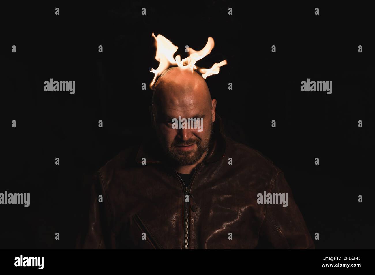 A bald man in a leather jacket with a burning head grins. Stock Photo
