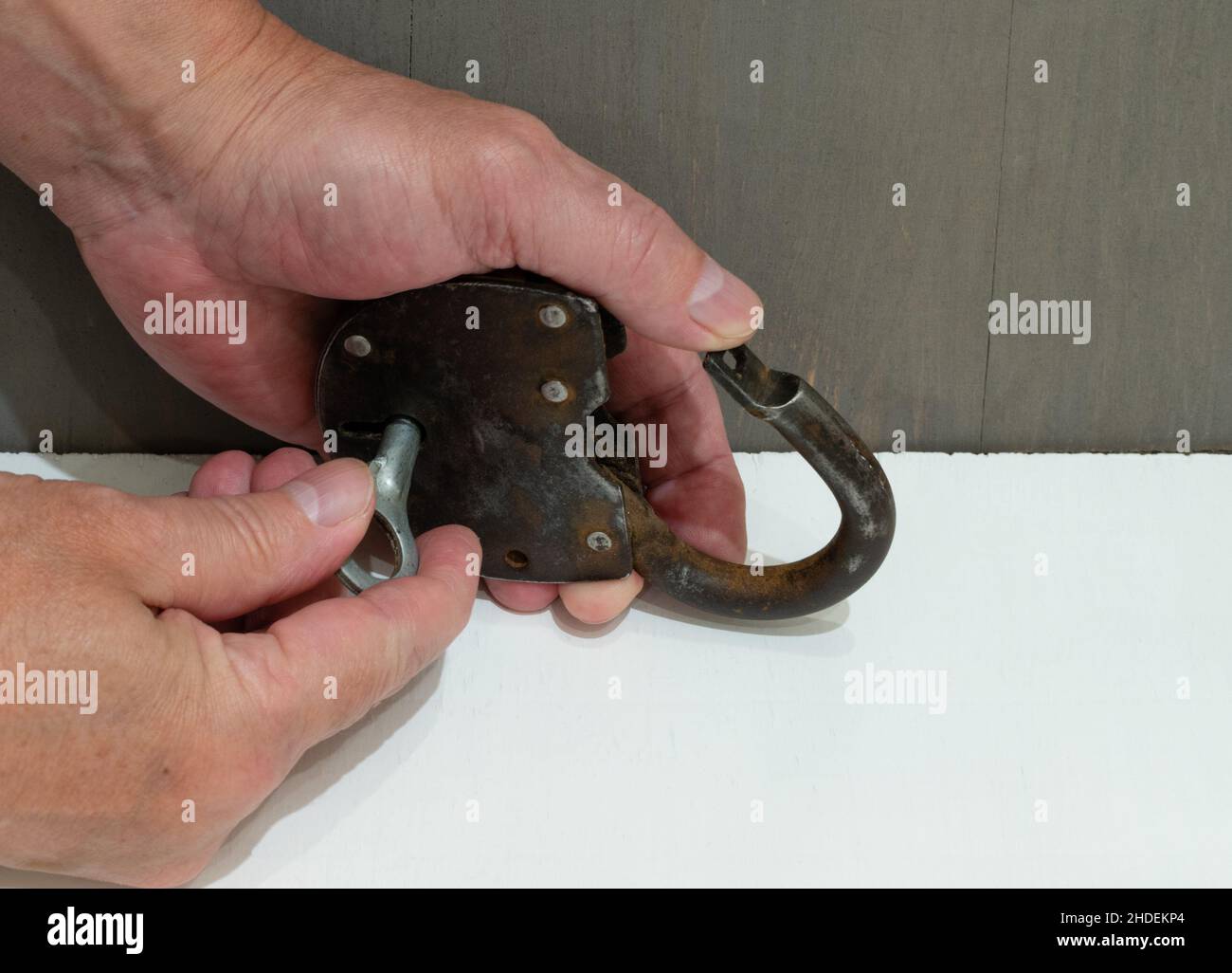 Old rusty padlock with key in hands close-up on white table Stock Photo