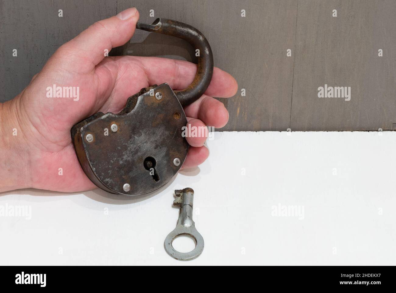Old rusty padlock with key in hand close-up on white table Stock Photo