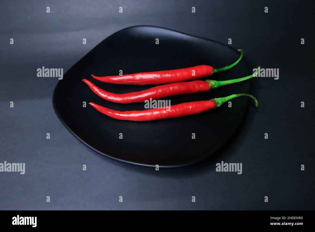 three chili peppers on a black plate Stock Photo