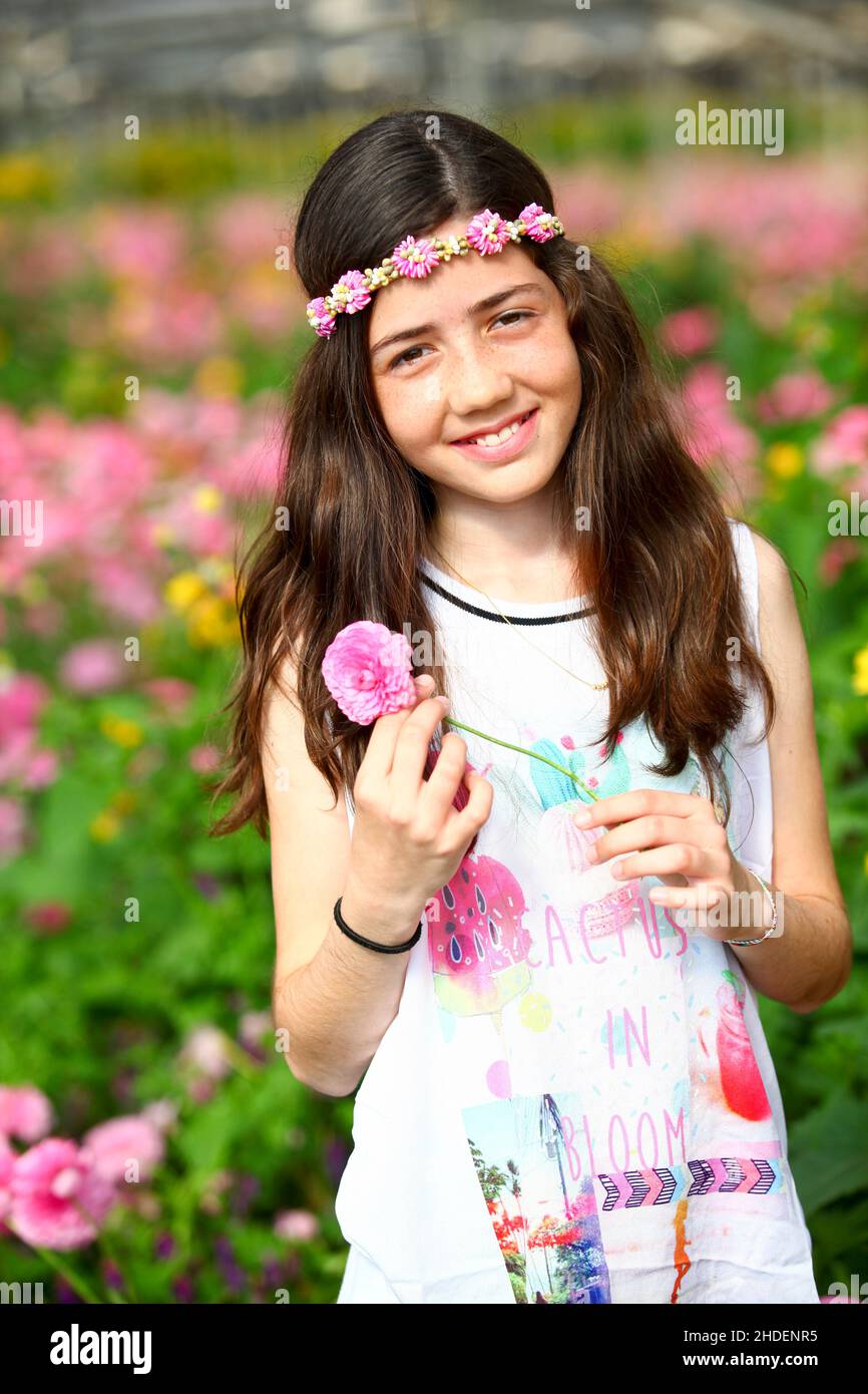 Young preteen girl of 12 in white dress in a hothouse of pink flowers Stock Photo