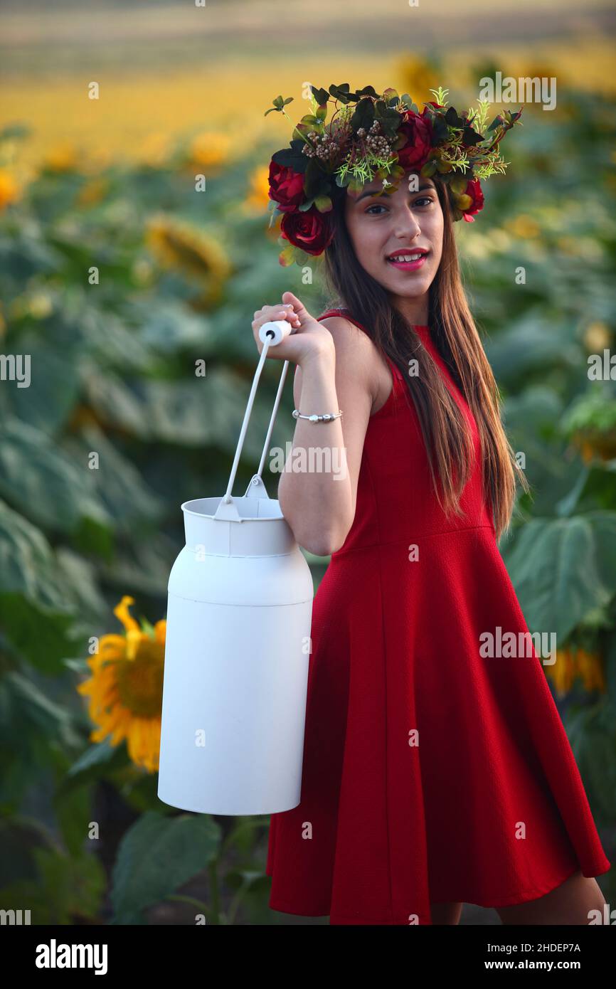 Preteen with wreath in a field of sunflowers carries a milk canister Stock Photo