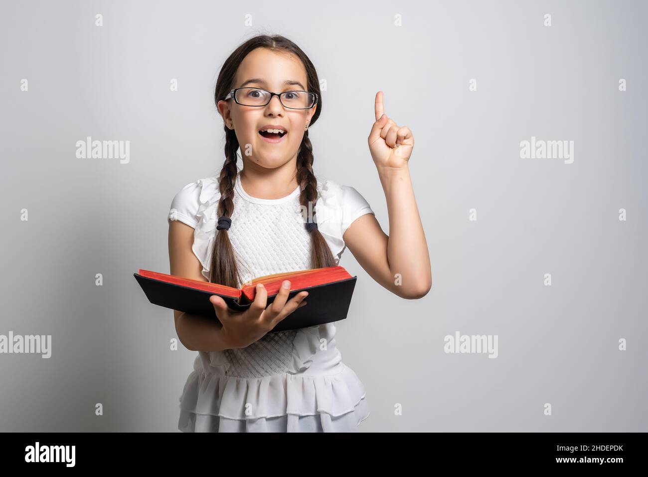 Lovely little girl standing and holding book over white background ...