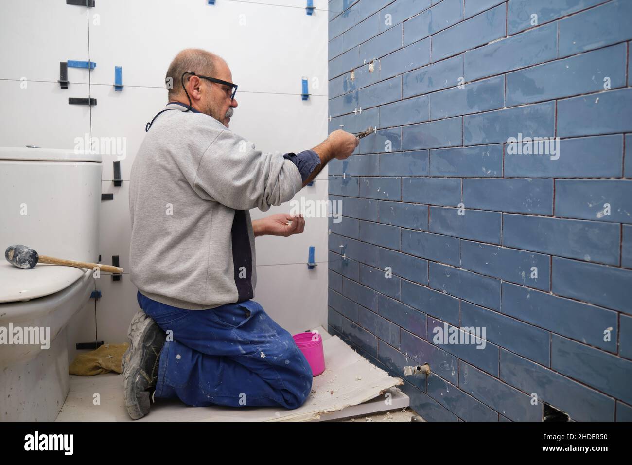 Senior constructor worker removing the separation between tiles on the wall. Stock Photo