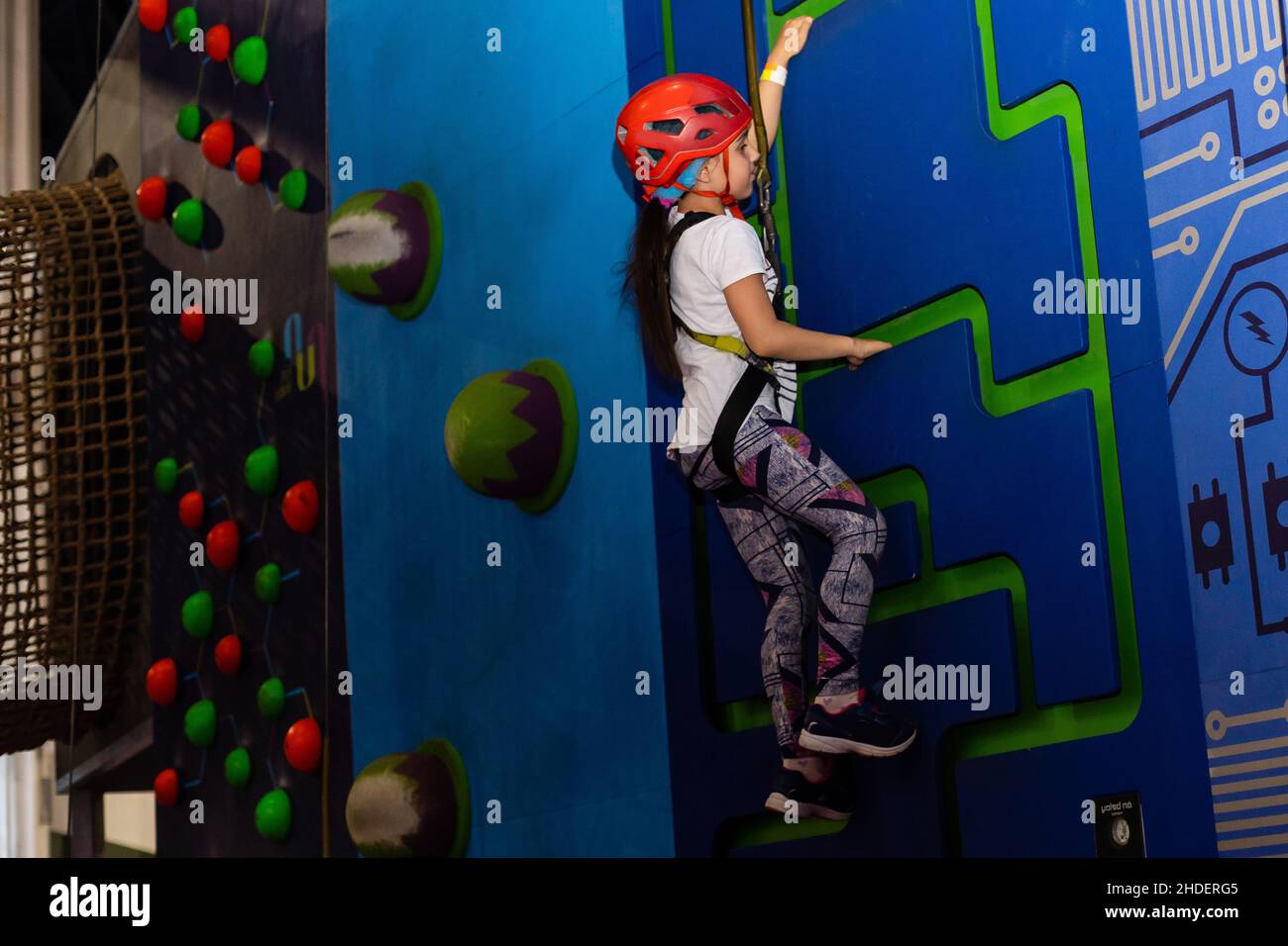Girl wearing in harness and safety equipment climbing on practical wall