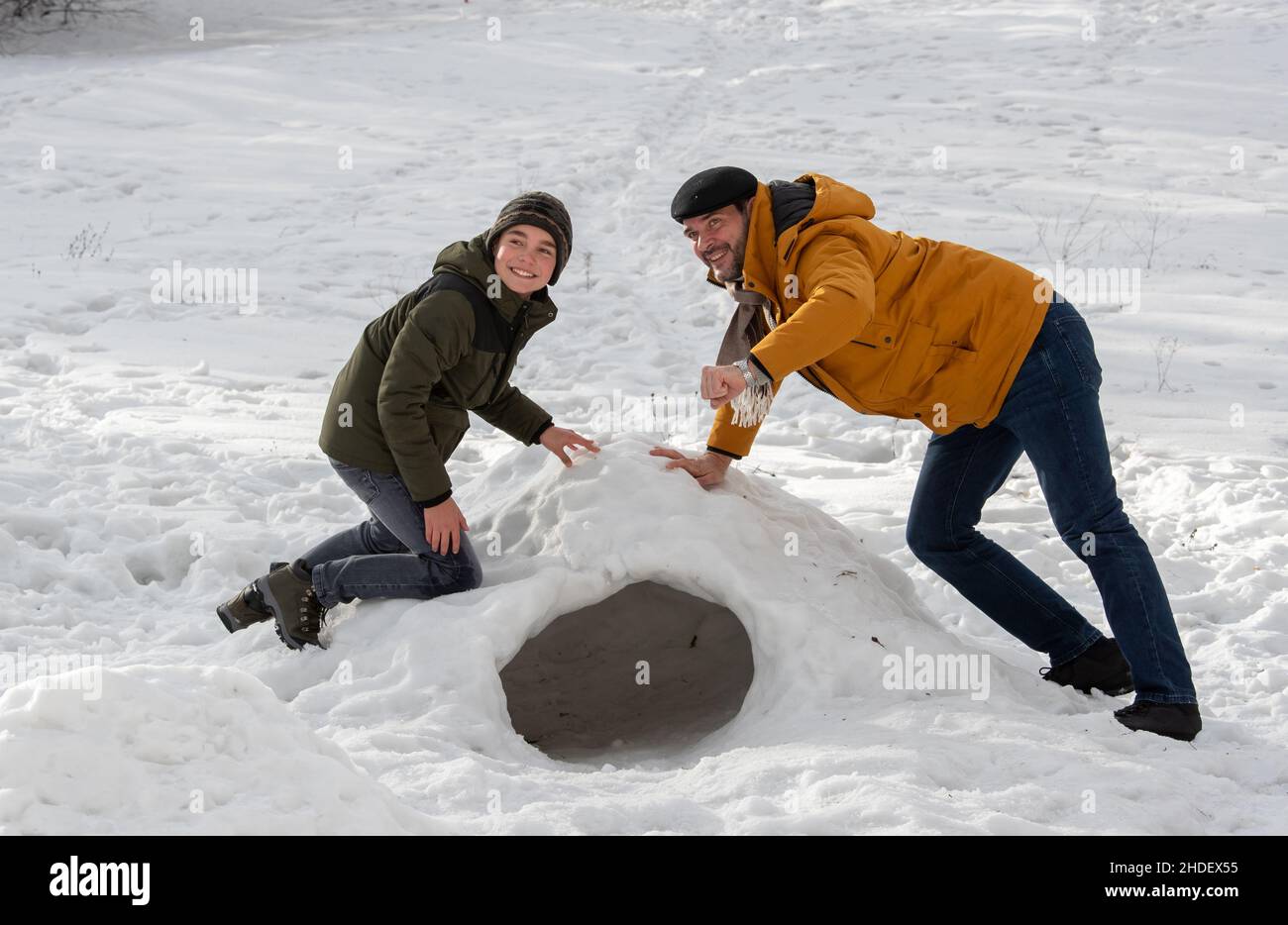 Father and son playing on snow making dome and shelter from cold in park on mountain during winter holidays Stock Photo