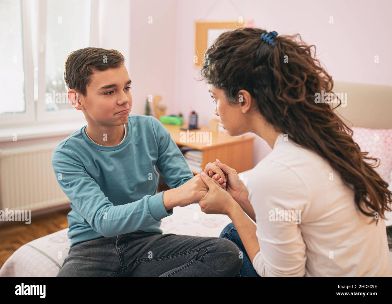 Mother holding kid for hands and having serious conversation but boy feels