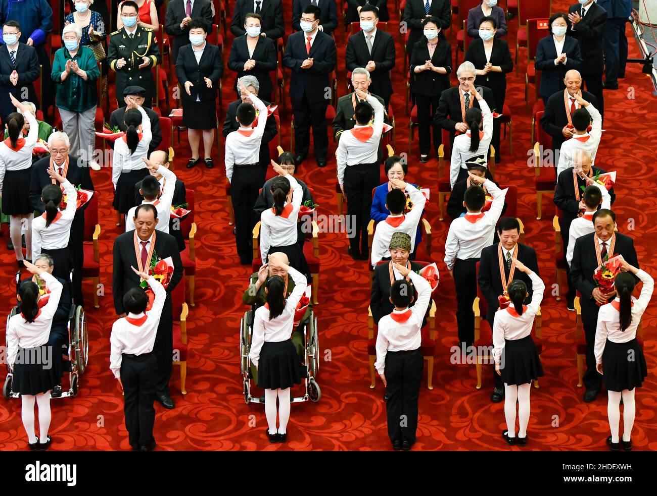 Beijing, China. 29th June, 2021. A group of children, who are members of the Chinese Young Pioneers, present flowers to recipients of the July 1 Medal and salute to them at the Great Hall of the People in Beijing, capital of China, June 29, 2021. Credit: Gao Jie/Xinhua/Alamy Live News Stock Photo