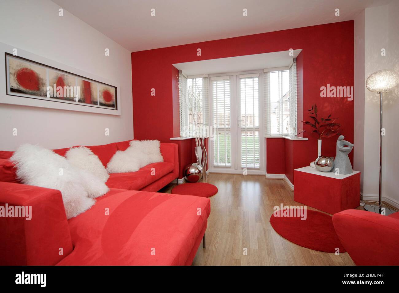 Modern lounge withwood effect laminate floor and corner sofa, chair,  furniture in scarlet red. Red decor. French doors. Stock Photo