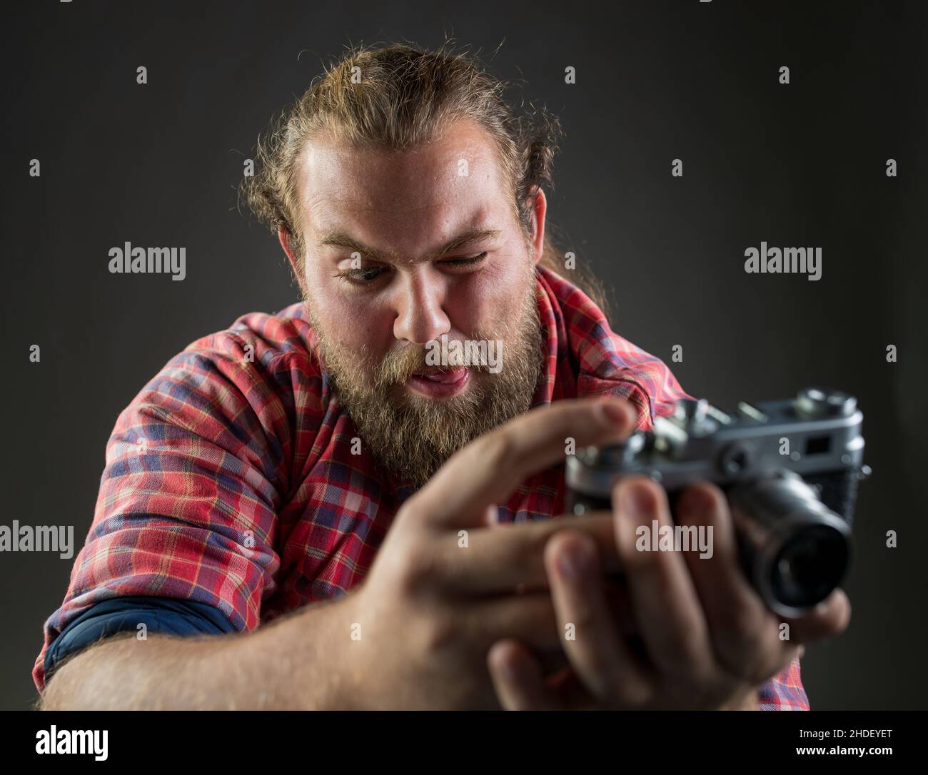 Young bearded man making funny facial expression while taking a photo with old-fashioned camera. Stock Photo