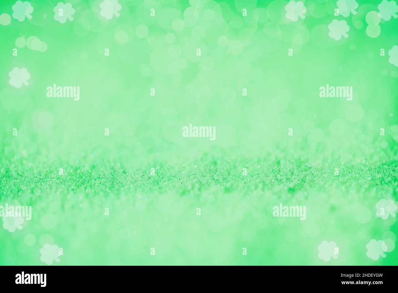 Beautiful bright blurred green glitter bokeh background with shamrock designs perfect for St. Patrick's Day. Stock Photo