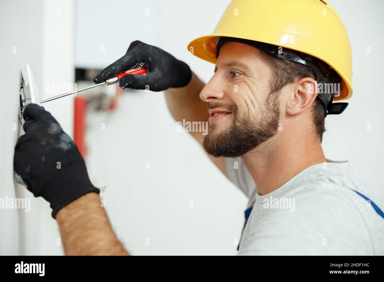 Smiling professional electrician in uniform replacing a socket in apartment after renovation work Stock Photo