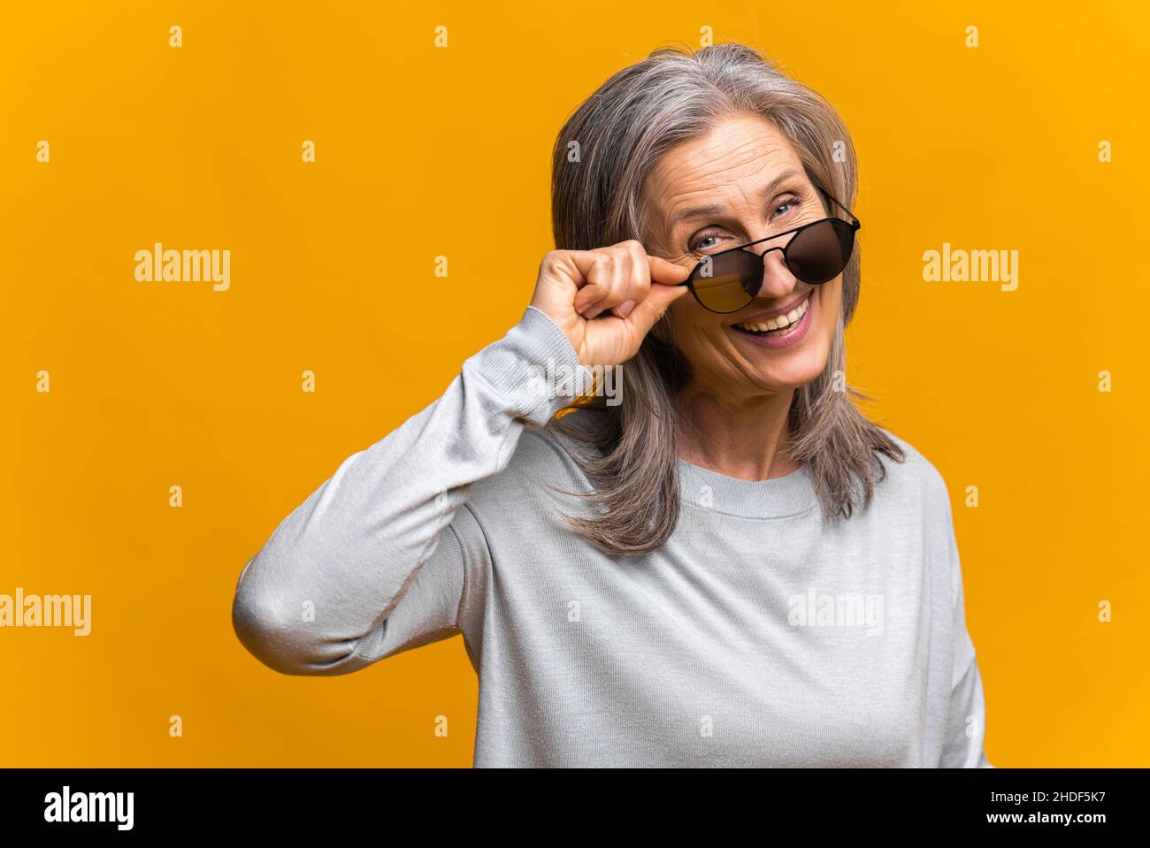 Photo of confident mature female model wears trendy sunglasses, prepares for date, isolated on yellow background, has fashion look Stock Photo