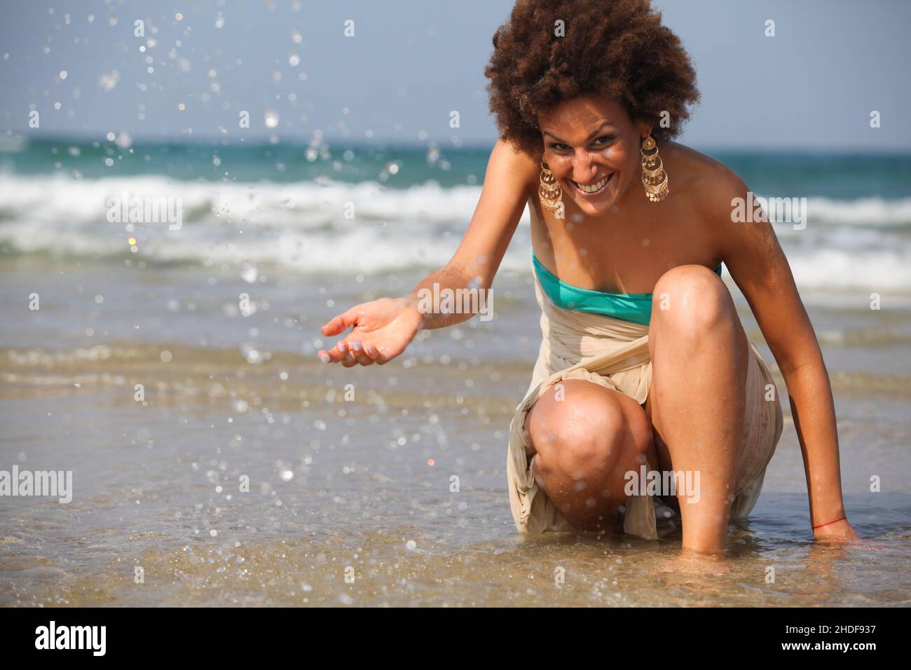 Happy excited 28 year old woman splashes sea water on the beach Stock Photo
