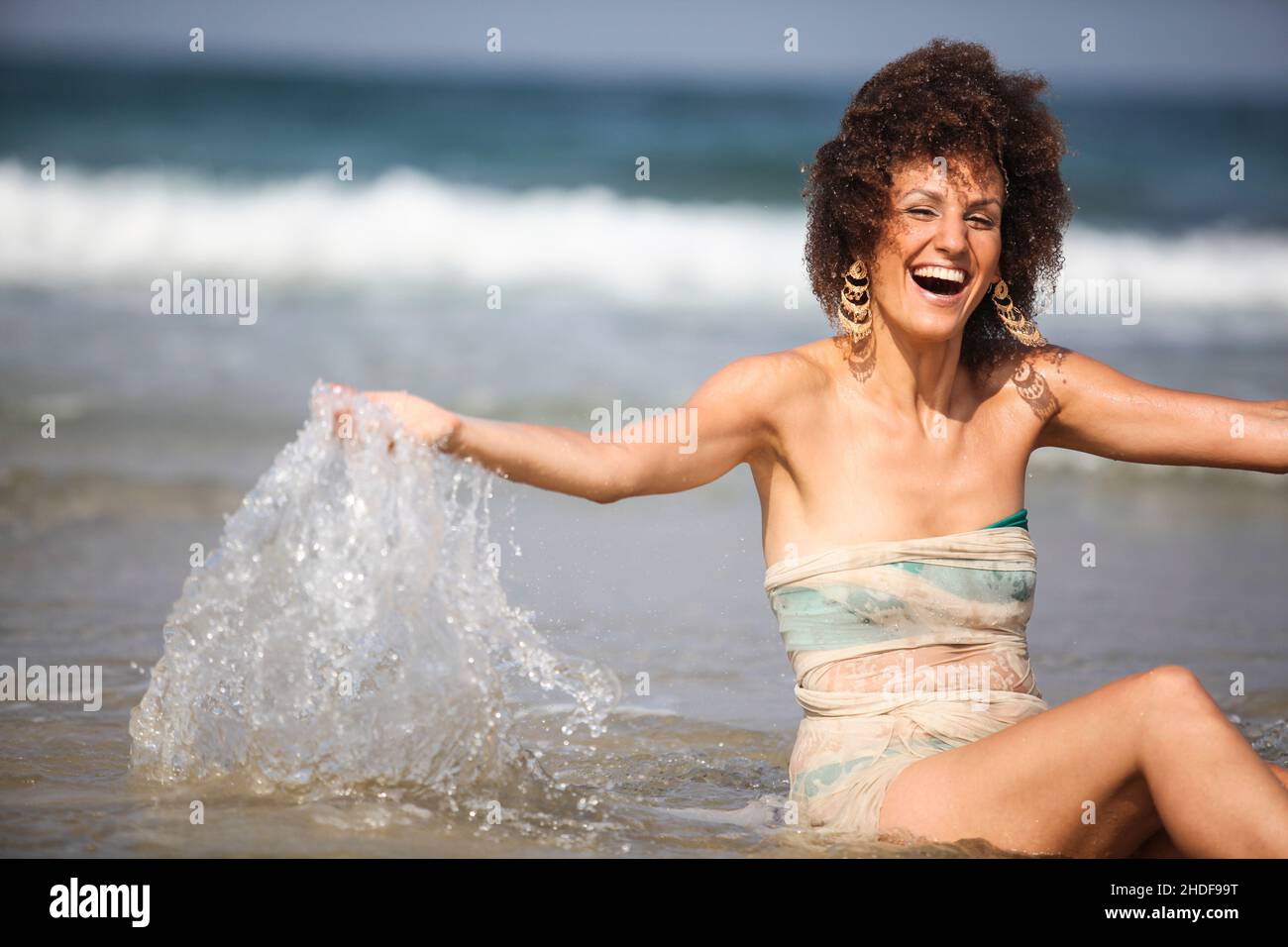 Happy excited 28 year old woman splashes sea water on the beach Stock Photo