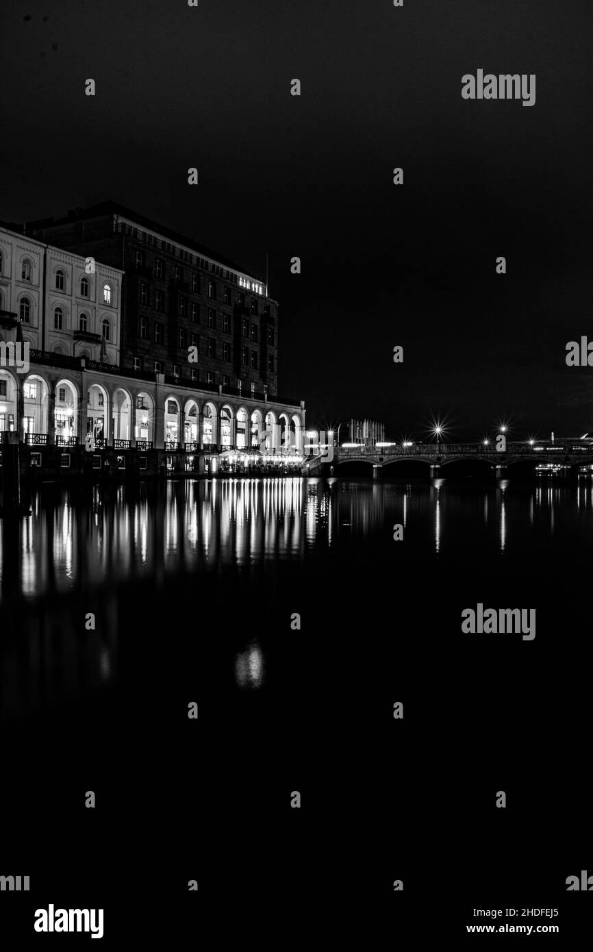 Grayscale shot of a city at night with lake in the foreground Stock Photo