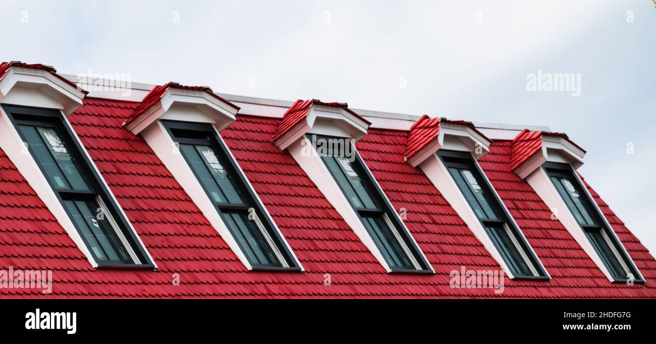 Row of red dormer roof windows against a cloudy sky Stock Photo