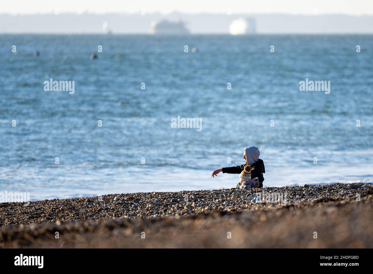 Shingle beach. Man with boy throwing pebbles into the sea, Hayling Island, Hampshire, UK Stock Photo