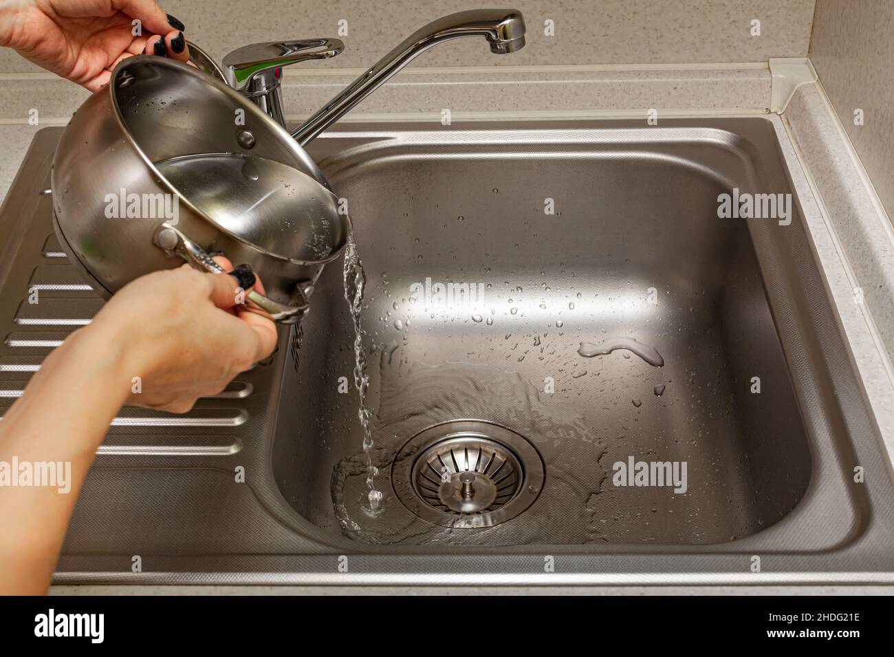 female hands pouring water from the pan into the sink in the kitchen Stock Photo