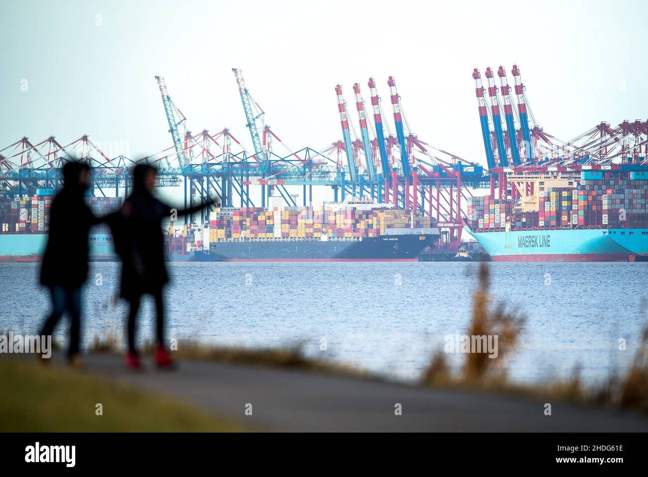 Nordenham, Germany. 06th Jan, 2022. Strollers walk along the banks of the Weser River, with Bremerhaven's industrial port in the background. Credit: Sina Schuldt/dpa/Alamy Live News Stock Photo