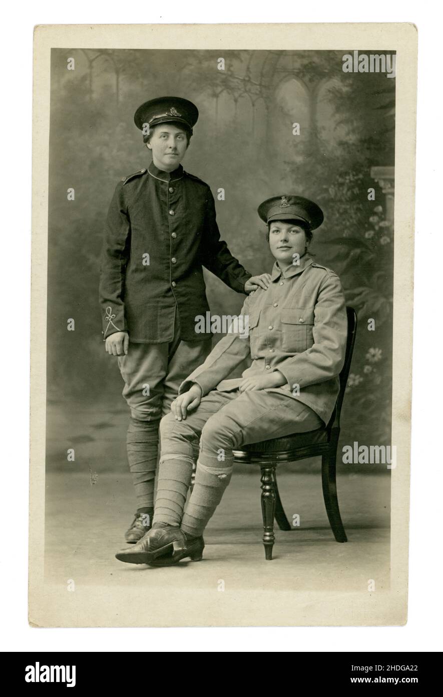 Original WW1 era studio portrait postcard of 2 young women dressed up in soldier's uniforms. Perhaps their boyfriend's uniforms. The woman on the left is wearing cap badge of the Royal Artillery, and the woman on the right is wearing one from the Wiltshire Regiment. From the studio of  H A Aylward of Alton, Hampshire. On reverse is  written ' August 1917, me and pal at Burkham'..Burkham is a hamlet in the large parish of Bentworth in East Hampshire, England and includes a large country house -  Burkham House. 1917, U.K. Stock Photo