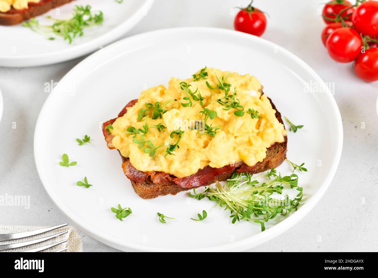Scrambled eggs with microgreen and bacon on bread, close up Stock Photo