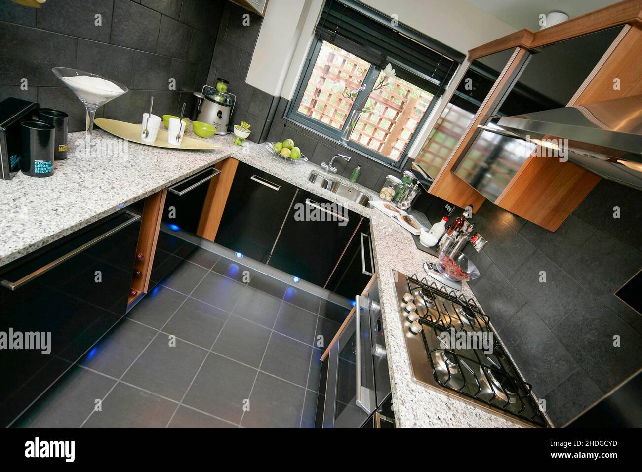 Modern small kitchen,black units,quartz worktop,plinth lighting,floor lighting,tiled floor. Stock Photo