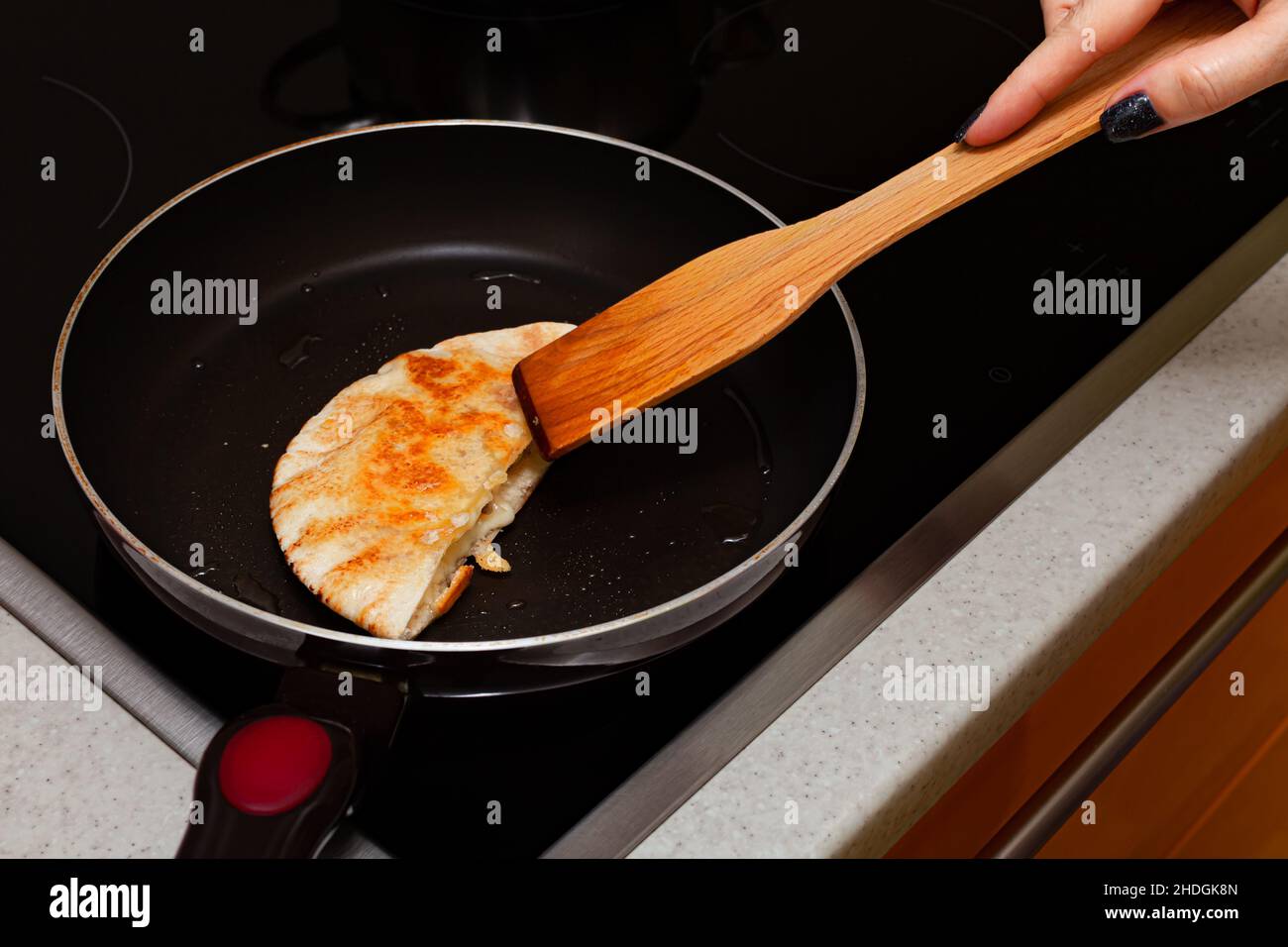 a woman's hand with a spatula turns a cake in a frying pan Stock Photo