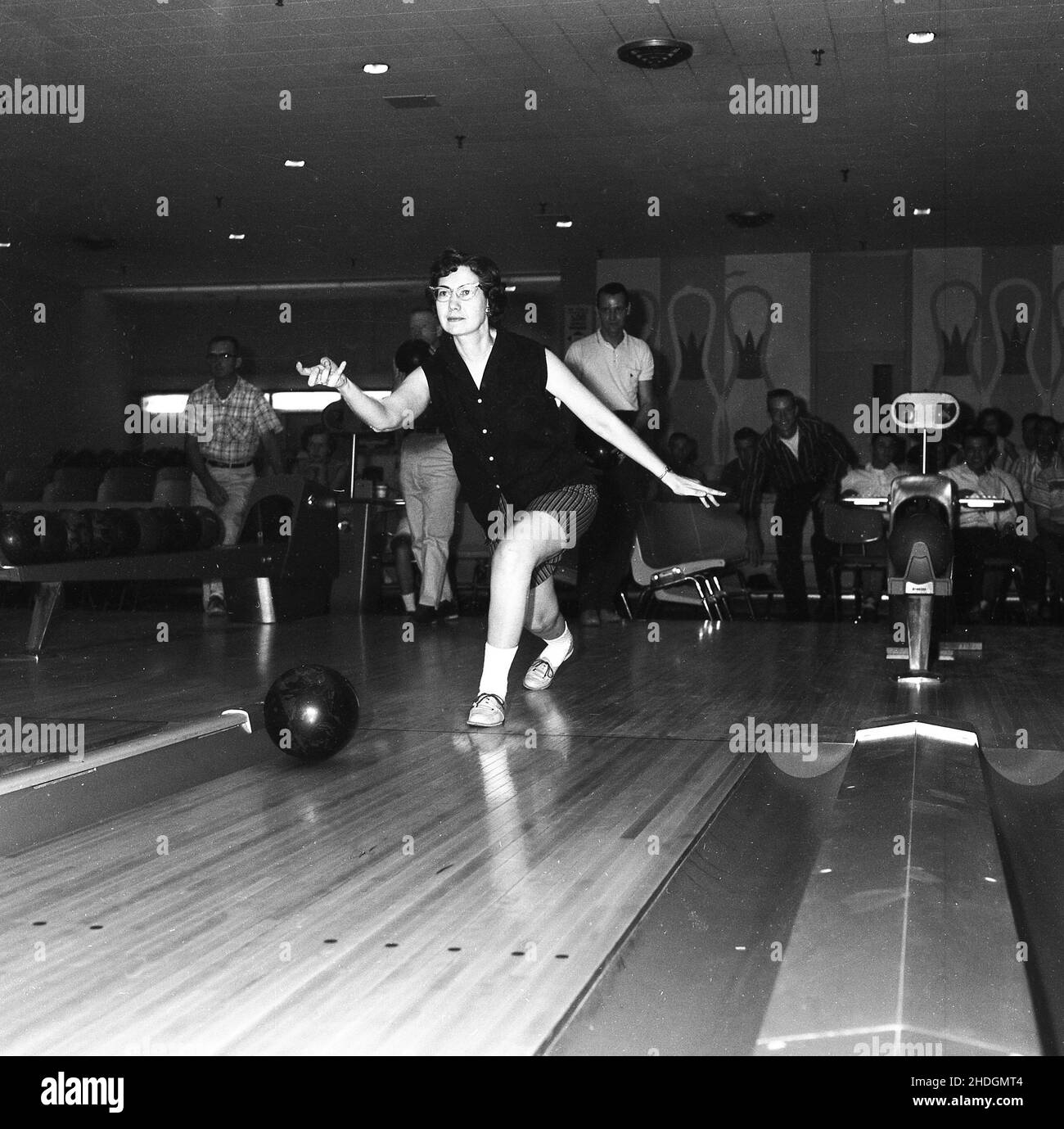 1960, historical, inside a ten-pin bowling hall, a woman player rolling a ball down a lane, Columbia, USA, showing good balance and technique.  Seen on the right is the gutter or channel, a trough shaped area, where the misplaced balls end up. In the 1950s and 60s, a popular lesiure pastime in the USA, tenpin was also a competitive sport, with an organised, competitive league structure, with both men and women teams. The Professional Bowlers Association of America (PBA) was founded in 1958. Stock Photo