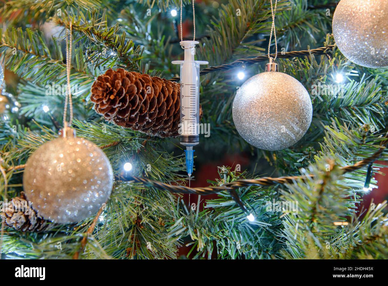 Coronavirus pandemic - A Covid-19 Booster Vaccine Syringe hanging on a Christmas tree Stock Photo