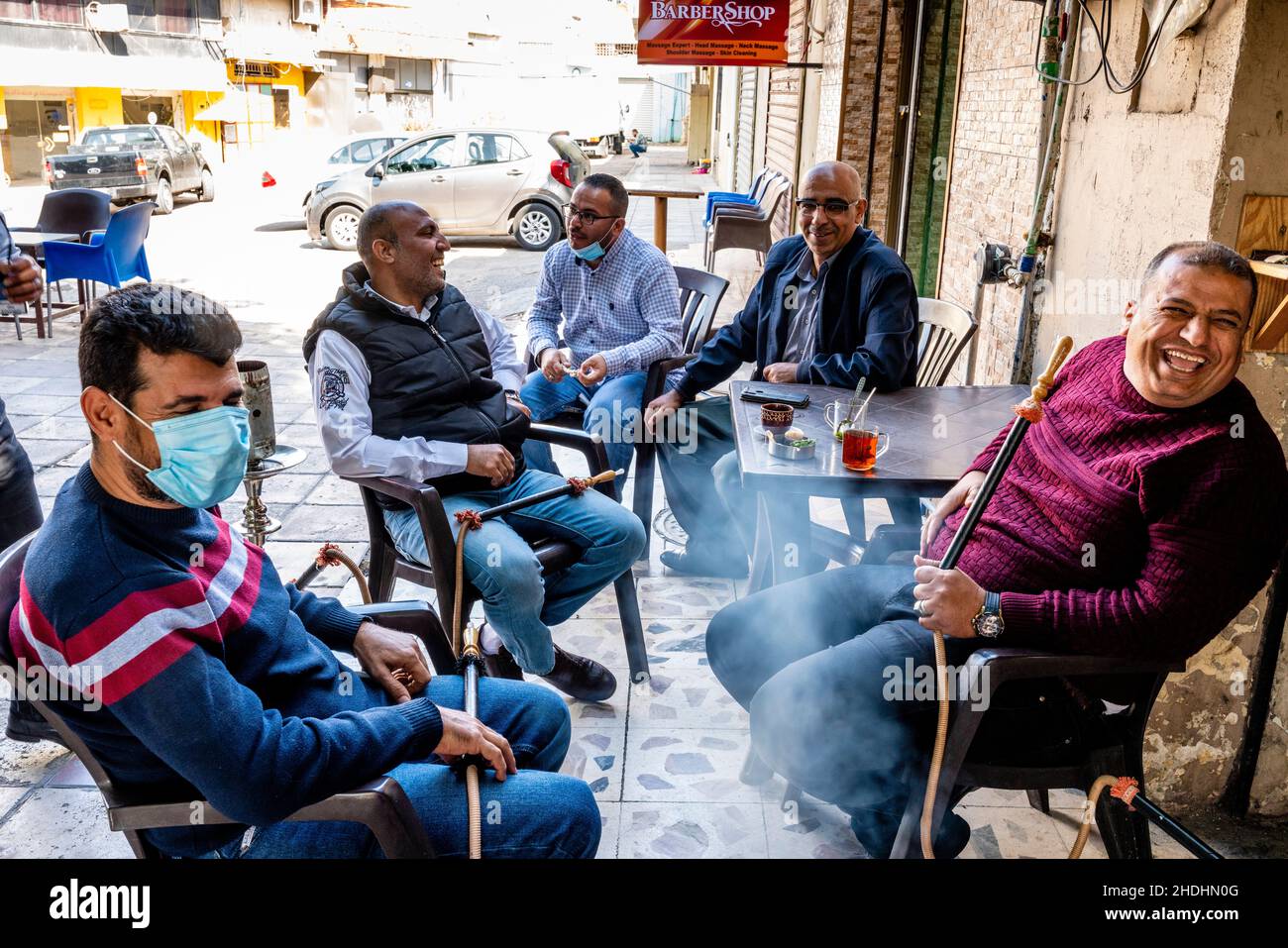 A Group Of Men Sit Around A Table Chatting and Smoking Shisha Pipes, Aqaba, Aqaba Governorate, Jordan. Stock Photo