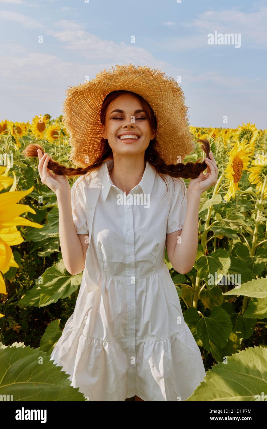 woman portrait in a straw hat in a white dress a field of sunflowers ...