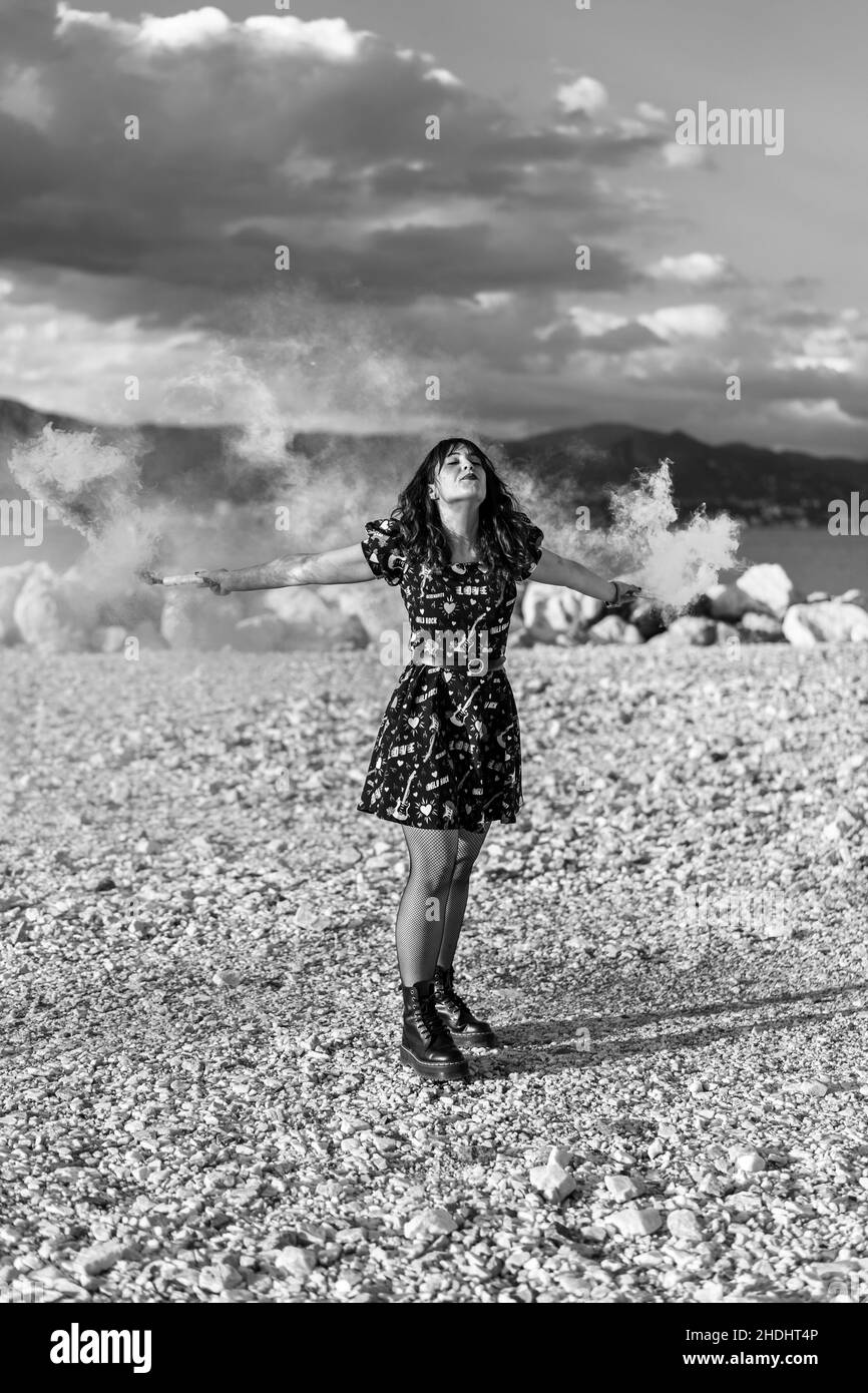 Vertical grayscale shot of a Caucasian woman in a dress spreading arms while posing Stock Photo