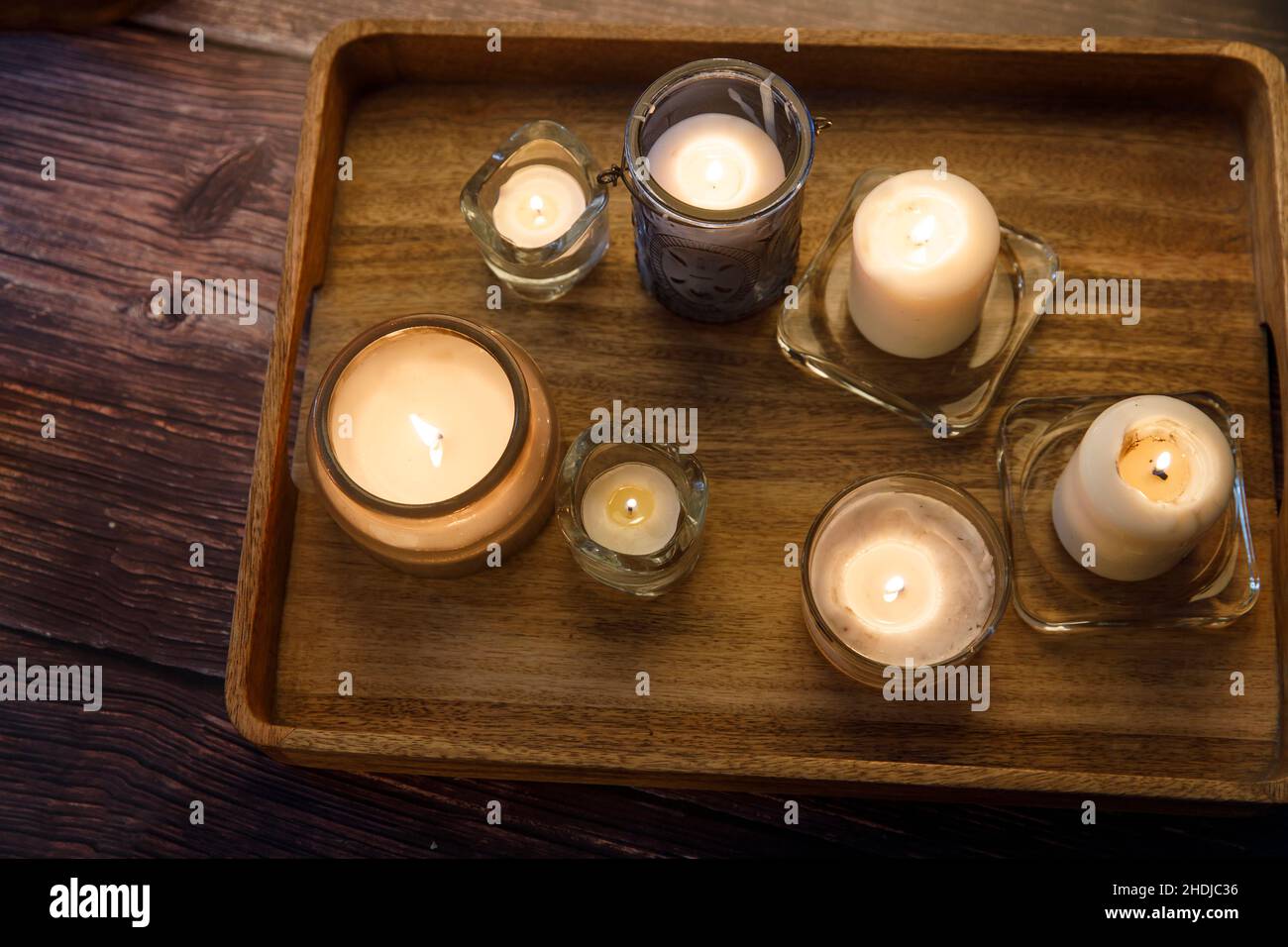 Interior and home cosiness concept. Top view. Lighted candles of various sizes and shapes in glass candlesticks on a wooden tray on the table Stock Photo