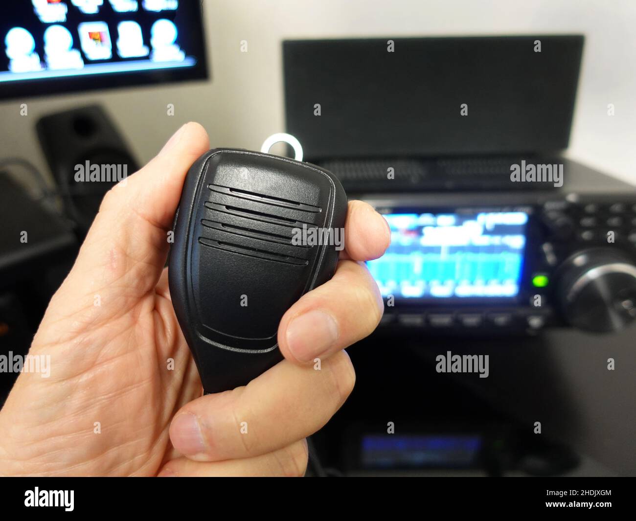 Man's hand holding a wired microphone with a ham radio defocused in background. Stock Photo