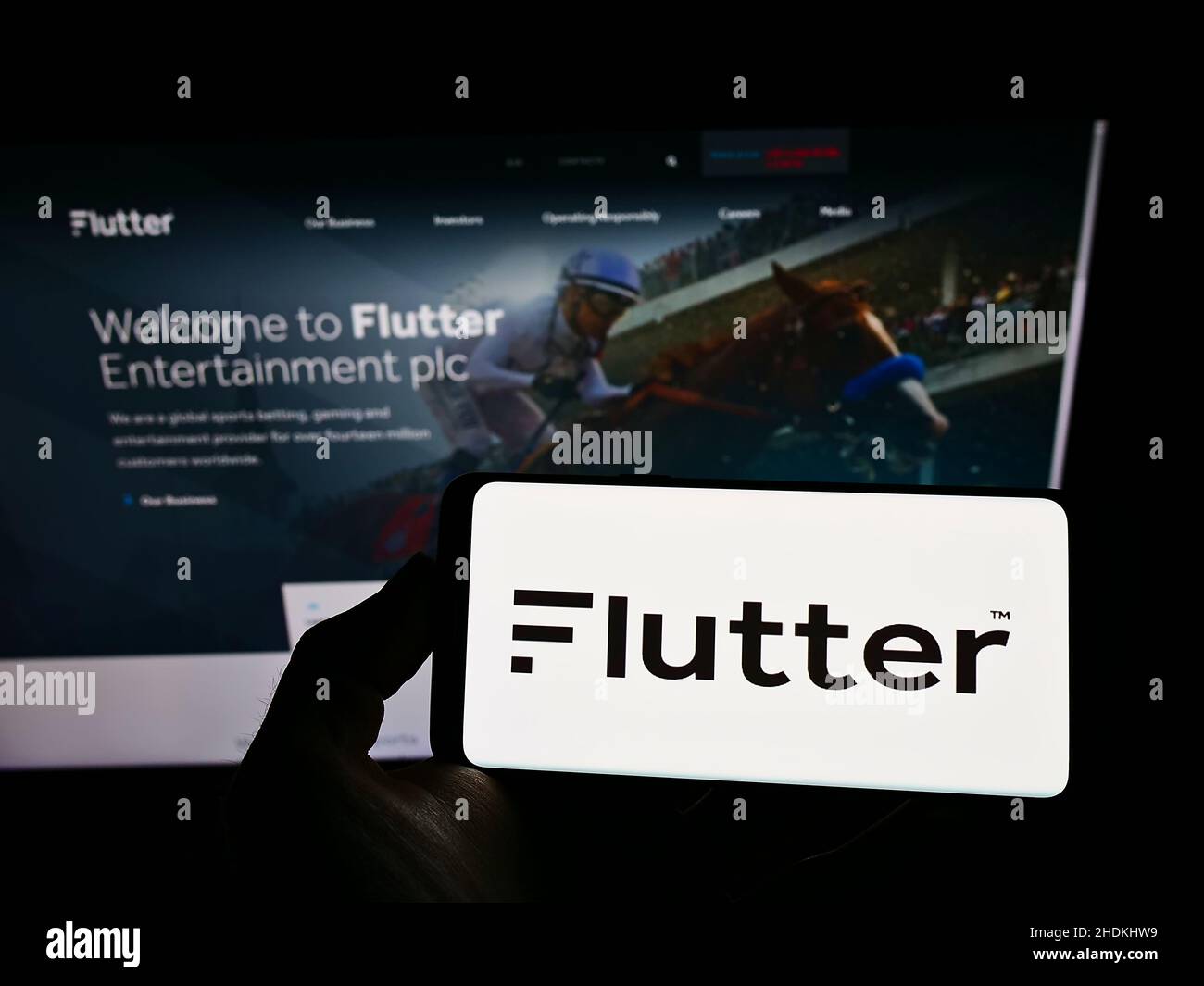 Person holding smartphone with logo of Irish bookmaking company Flutter Entertainment plc on screen in front of website. Focus on phone display. Stock Photo