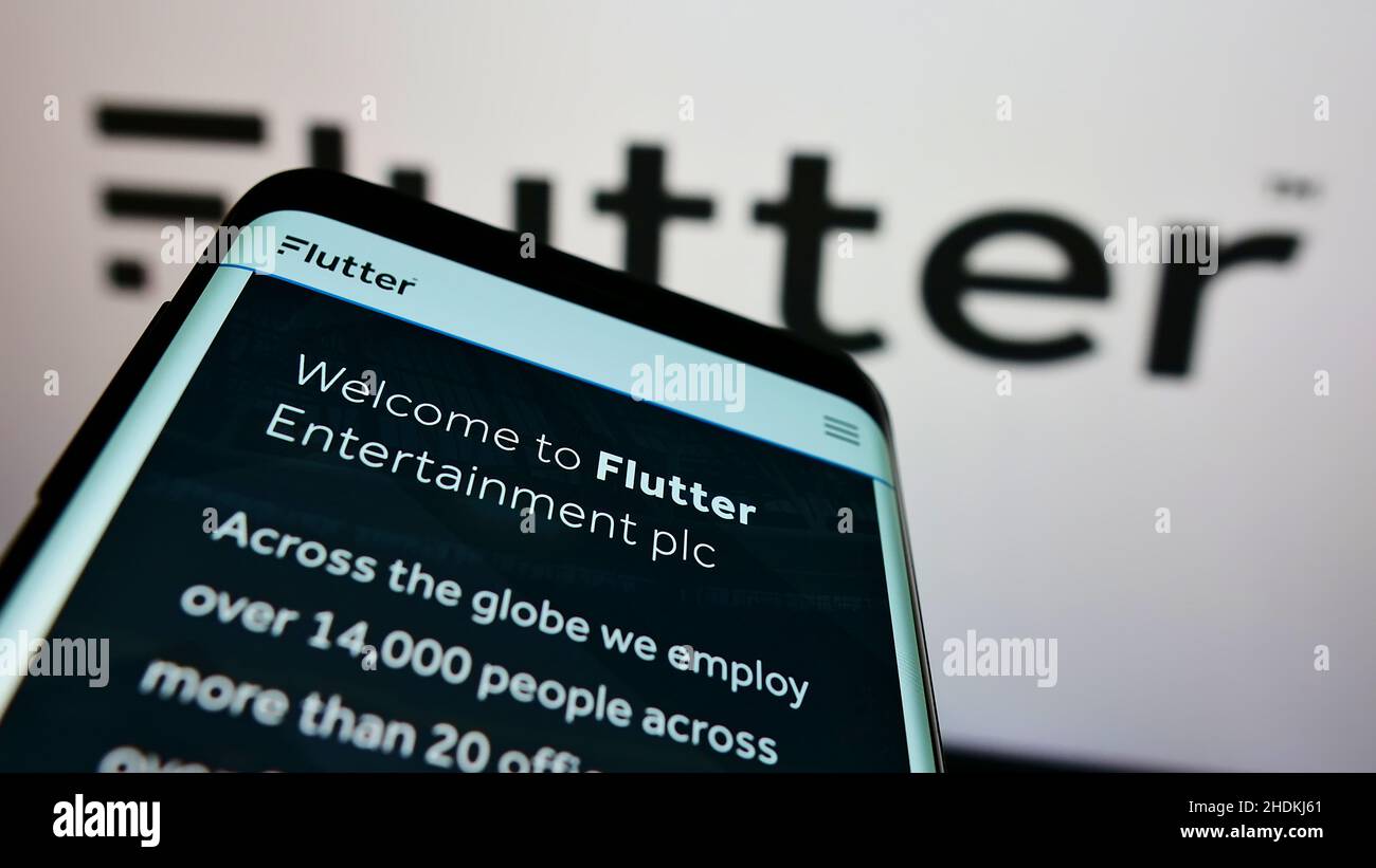 Smartphone with website of Irish bookmaking company Flutter Entertainment plc on screen in front of logo. Focus on top-left of phone display. Stock Photo