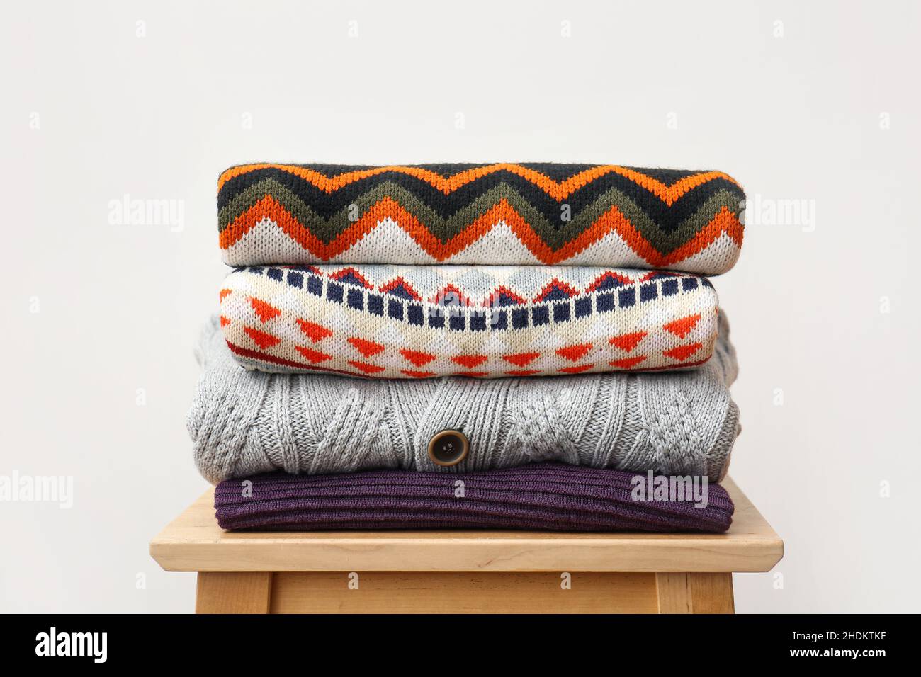 Stack of stylish sweaters on wooden stool against light background Stock Photo