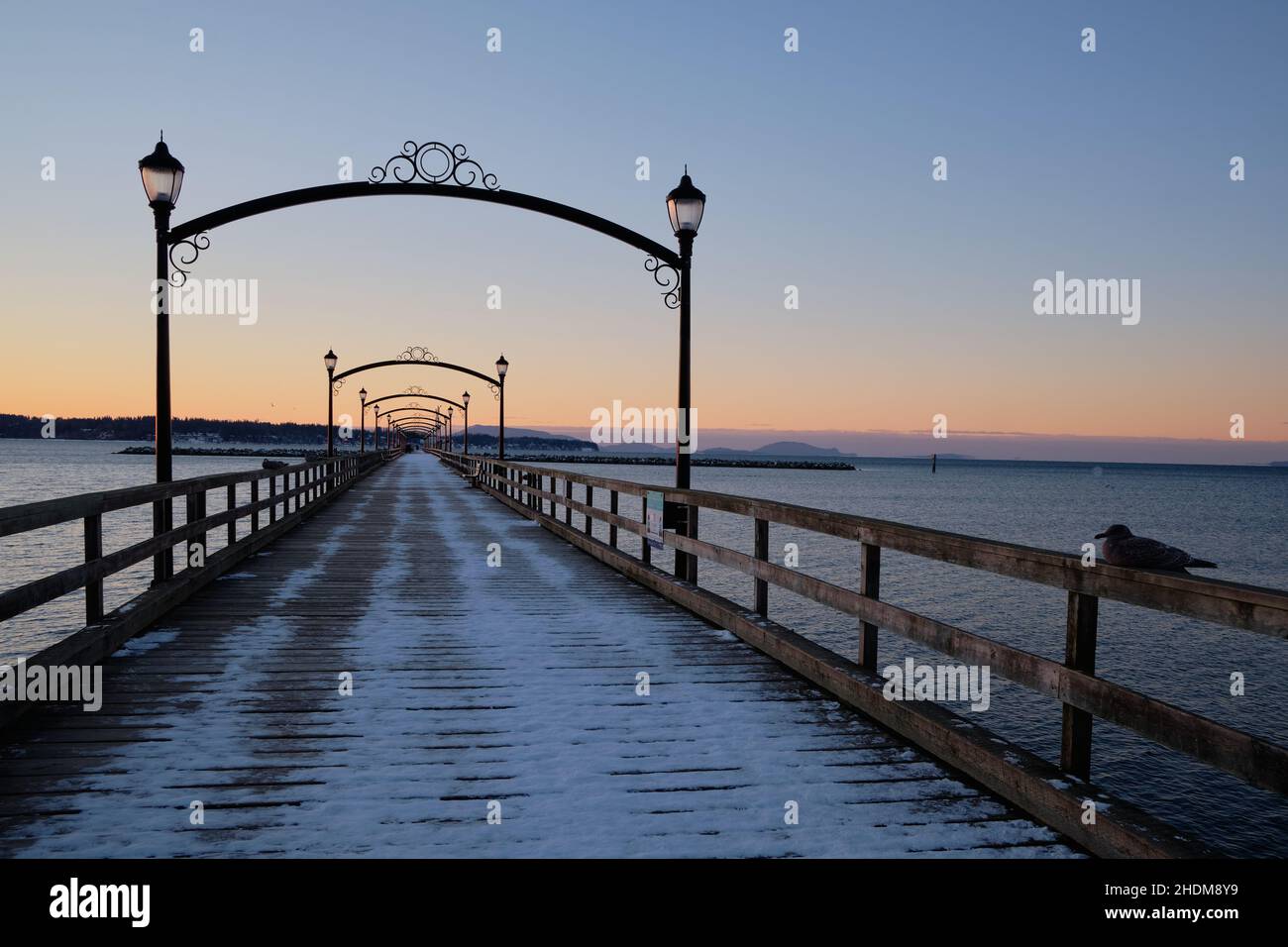 Thin covering of snow frosts wooden planks of White Rock's pier as soft pre-dawn light spreads over the scene on this quiet, cold, winter morning. Stock Photo