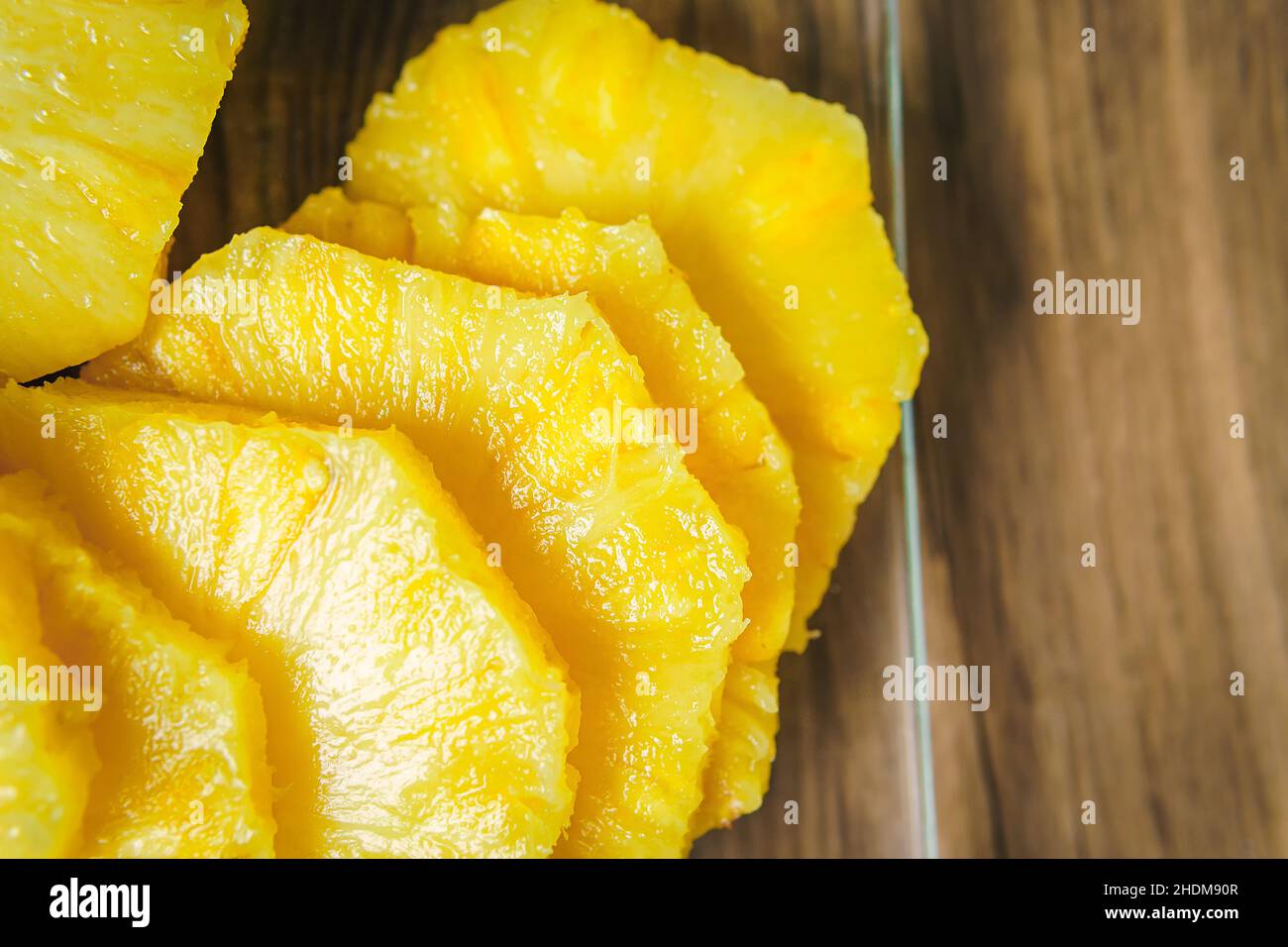 Close-up of a young woman's hands cutting a juicy pineapple with a chef's knife on a wooden table in a kitchen. Stock Photo