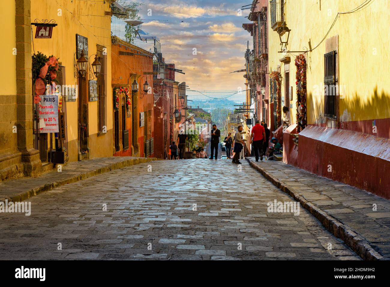 Sun setting on busy cobblestone street in the El Centro off the El Jardin with shops and cafes in the colonial city of San Miguel de Allende, MX Stock Photo