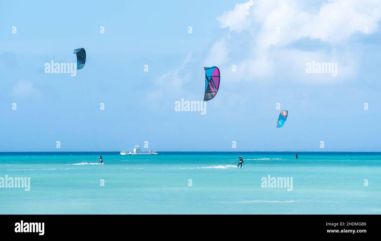 Kite boarders riding the wind on the bright turquoise Caribbean Sea waters off of Hadicurari Beach in Aruba. Stock Photo