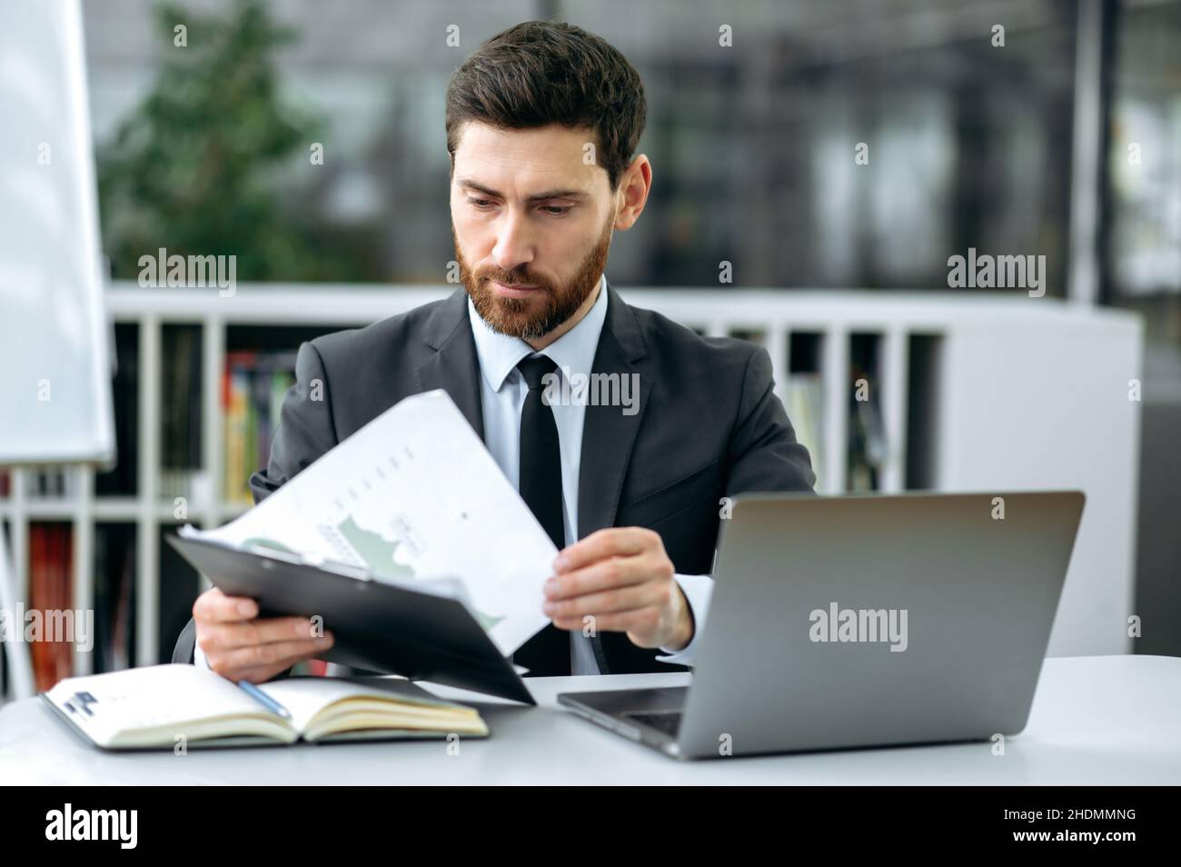 Smart confident caucasian bearded businessperson, ceo of company, top manager, financial expert, sits in modern office, concentrated studies financial documents, plans a development business strategy Stock Photo