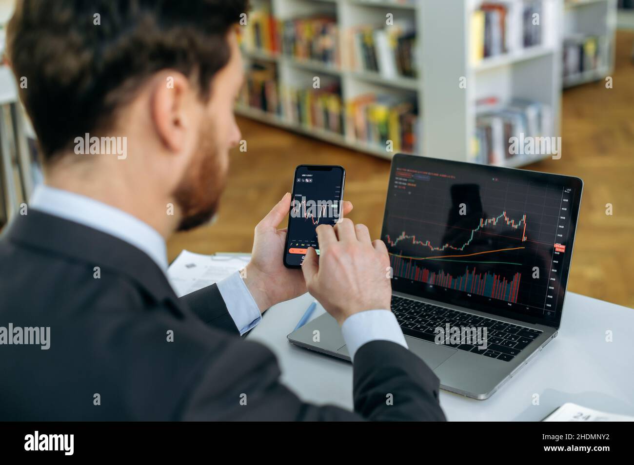 Exchange market. Smart man investor and crypto trader, using laptop and cellphone, analyzes charts of trading in stock market and digital cryptocurrency exchange,conducts analysis,trading crypto coins Stock Photo