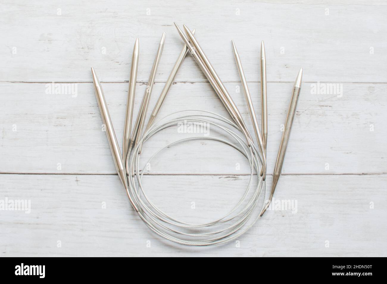 Circular knitting needles in different lengths on a light wooden surface Stock Photo