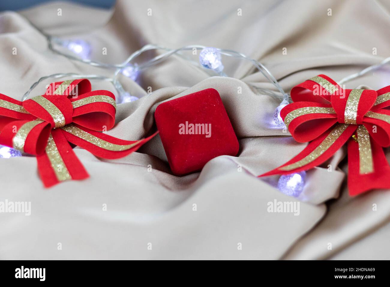 A closeup of a red jewelry box surrounded by decorative ribbons and bows on a silk fabric Stock Photo