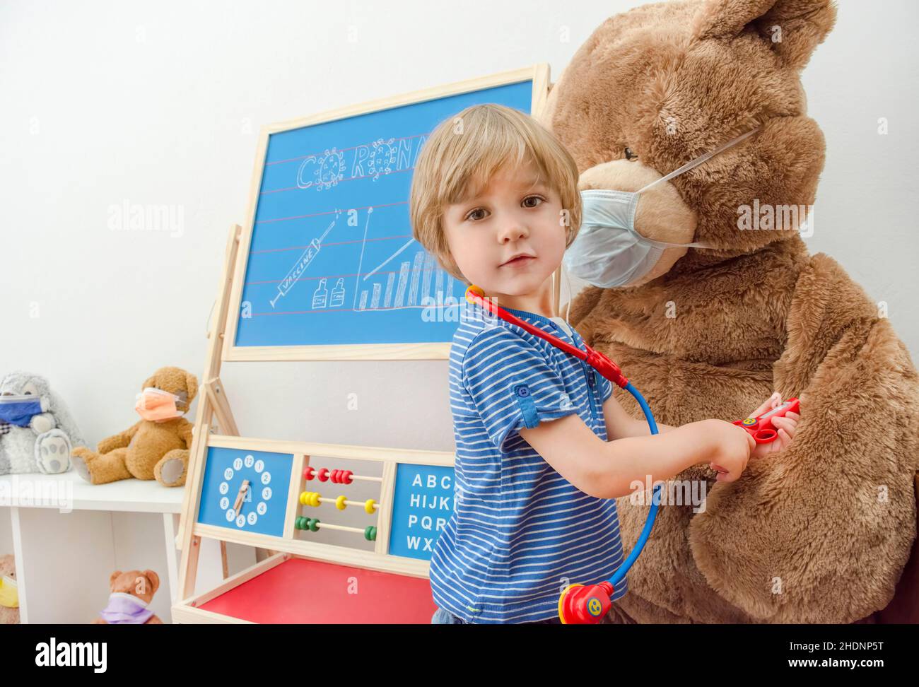 Cute child boy in home quarantine playing doctor with toys wearing medical masks, role playing during coronavirus pandemic lock down Stock Photo