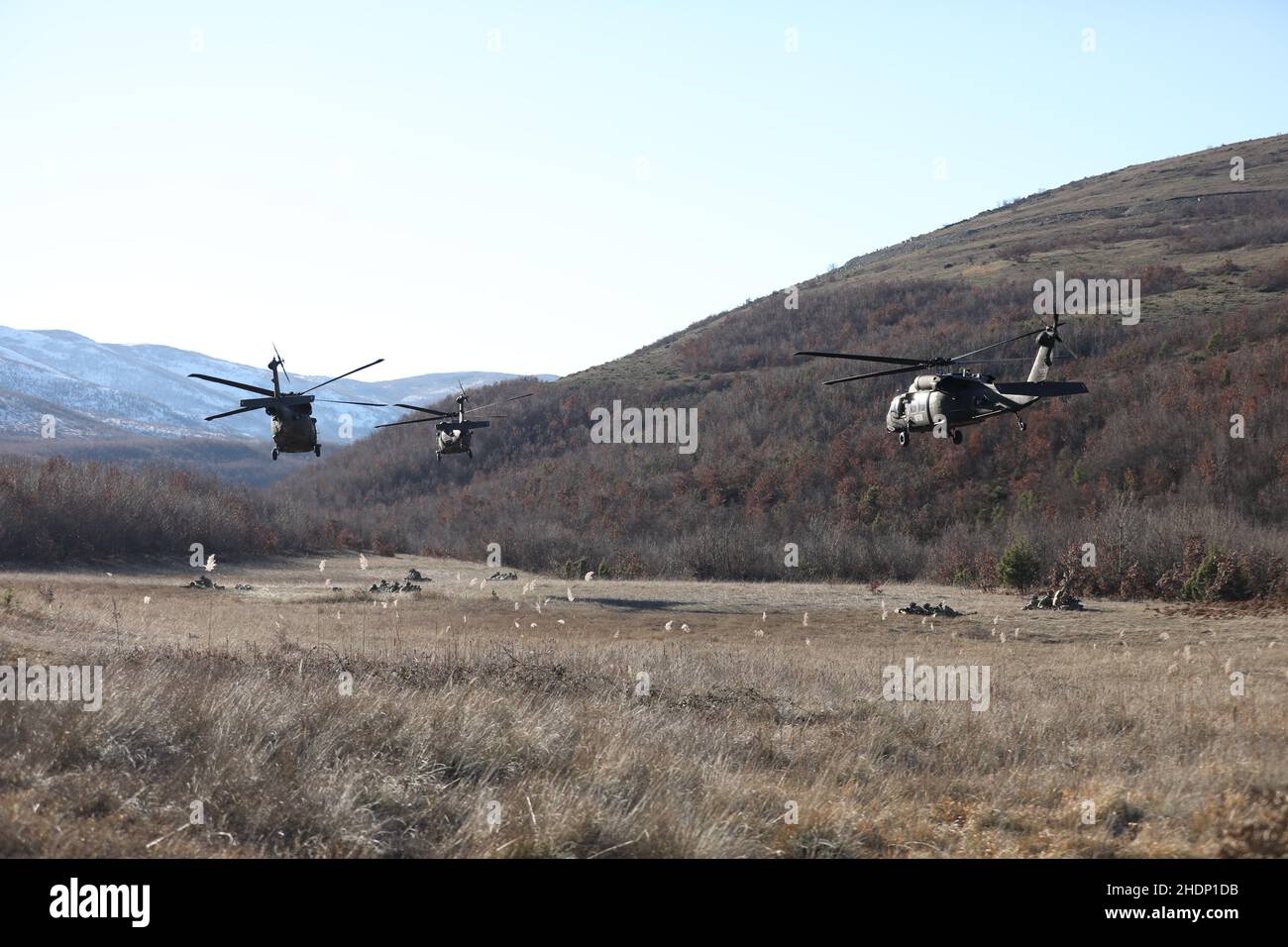 U.S. Army UH-60L Blackhawks belonging to A Company, 1st Battalion 169th Aviation Regiment take off from a landing zone while troopers belonging to 1st Squadron 172nd Cavalry Regiment (Mountain) pull security in the Babaj Boks Training Area, Kosovo December 21, 2021. The soldiers were participating in 'Alpine Swarm', a training exercise to maintain readiness for all contingencies while enhancing multi-national interoperability. This image was electronically cropped and ethically enhanced to emphasize the subject and does not misrepresent the subject or the original image in any way. (U.S. Army Stock Photo